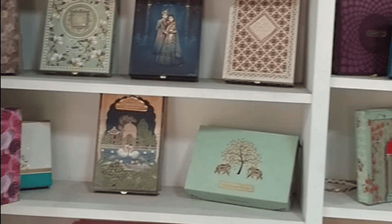 Artistic luxury sweets and invitation boxes displayed on white shelves, featuring floral and royal-themed packaging designs