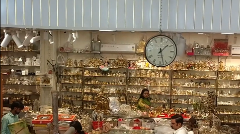 Devotional store in Vaishali Nagar Jaipur with shelves full of God murtis, brass idols, pooja samagri and gift items, with customers shopping at the counter under a large wall clock